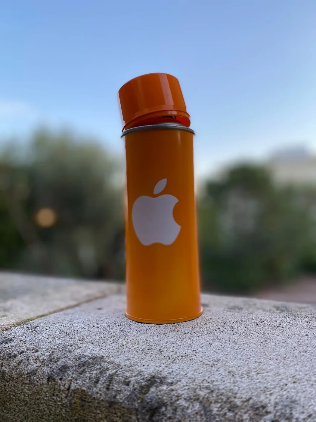 Petit extincteur orange personnalisé au logo Apple blanc, posé sur un muret en extérieur — Art'cade Design Nice
