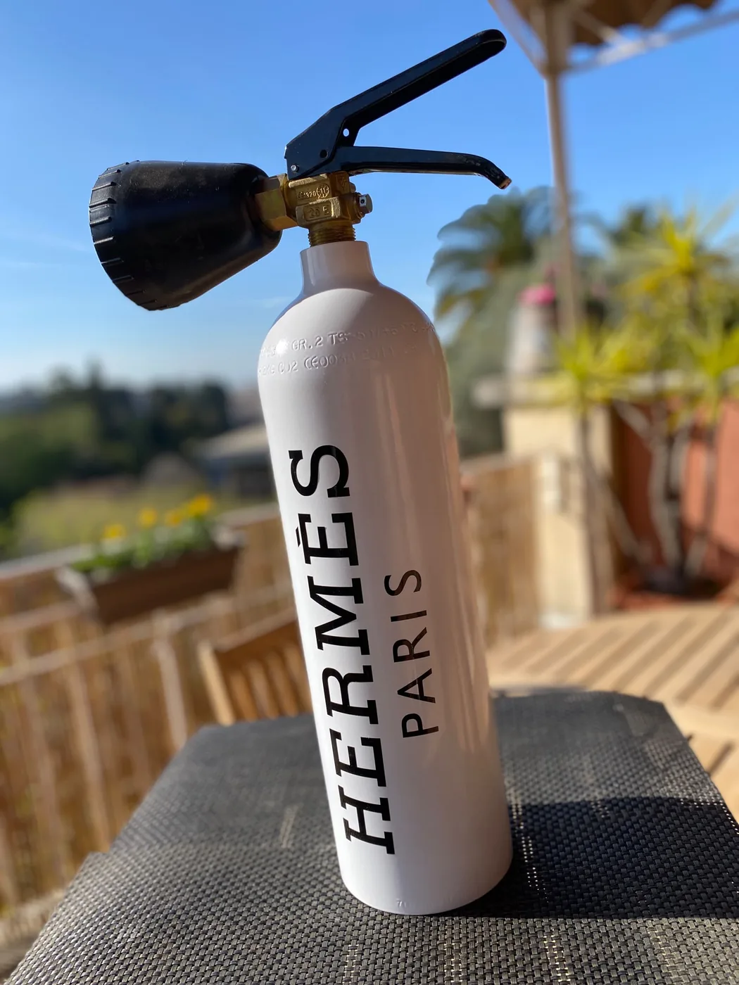 Extincteur blanc personnalisé au lettrage noir Hermès Paris, photographié en extérieur sur une terrasse ensoleillée — Art'cade Design Nice