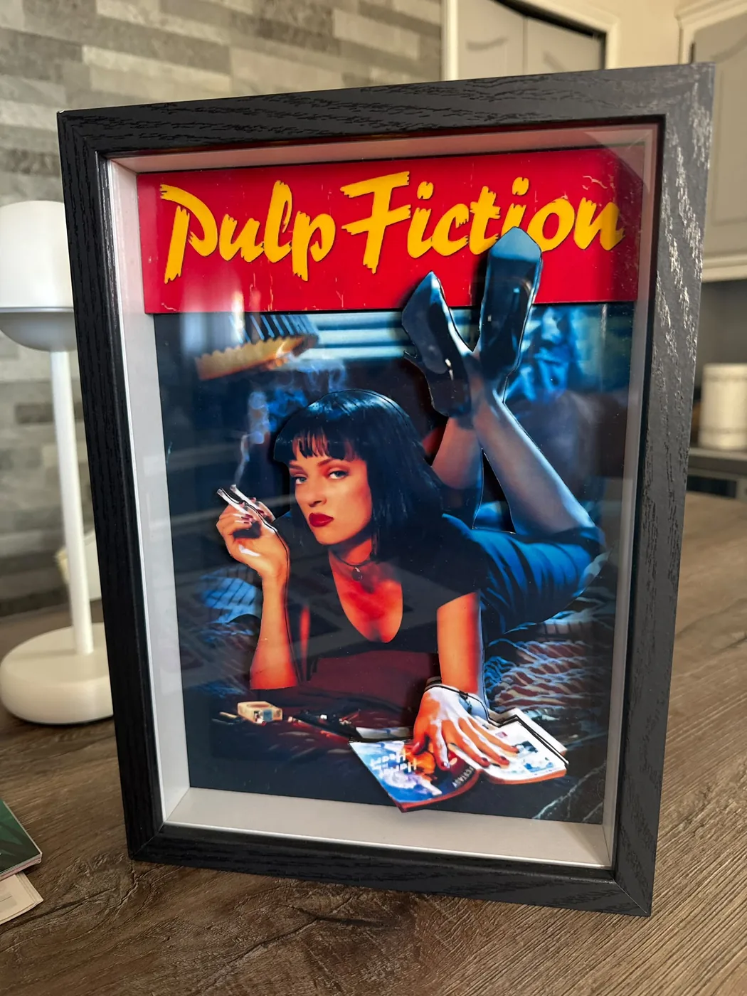 Cadre relief A4 en portrait : l'affiche de Pulp Fiction reconstituée en relief dans un cadre noir, debout sur une table en bois.