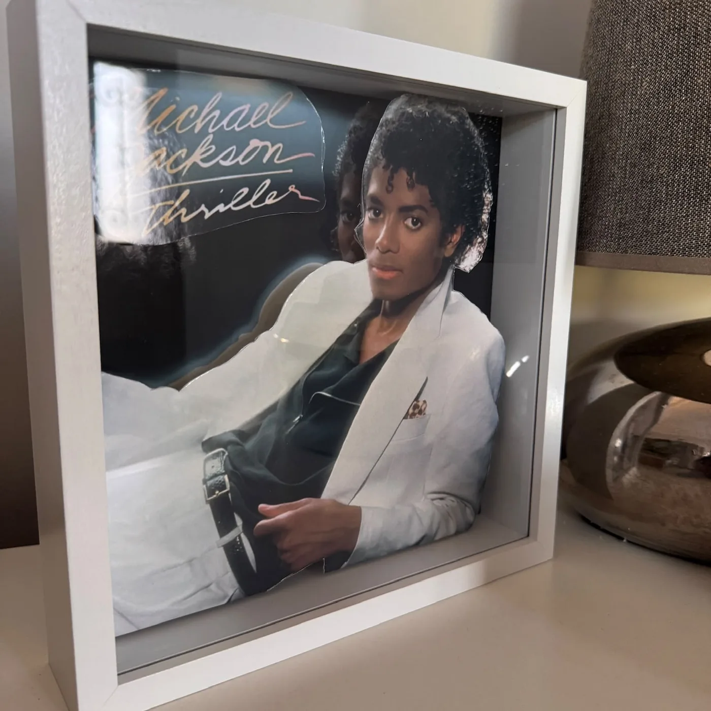 Cadre relief carré : la pochette de l'album Thriller de Michael Jackson reconstituée en relief dans une boîte-cadre blanche, posée sur une table d'appoint.