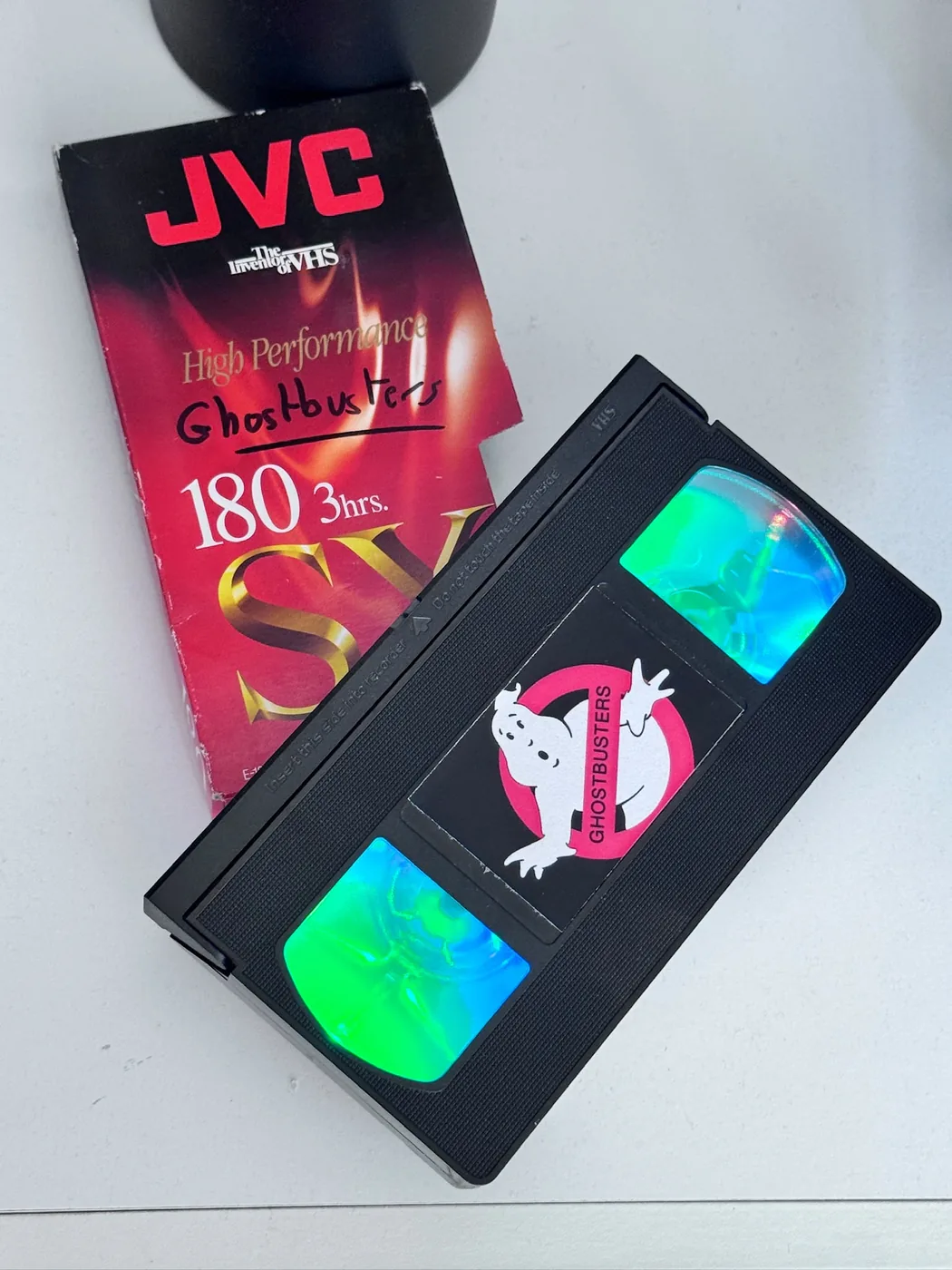 Une cassette VHS JVC habillée d'une étiquette Ghostbusters, posée à côté de sa jaquette.